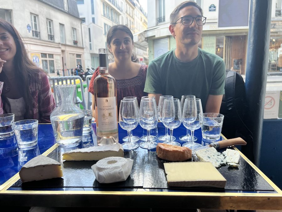 This is an image of a tour group surrounding a table with wine and cheese. They look like they are getting ready for a tasting. This is one of the top Paris tours for food lovers in North Marais.
