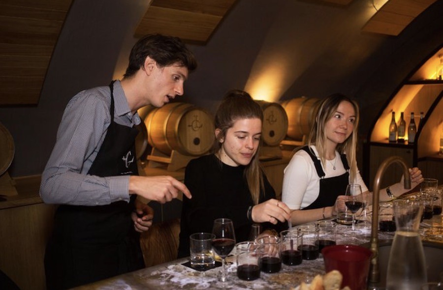 This is an image of a wine-making class where people are mixing flavours to create a taste they like. The teacher is standing next to them explaining instructions. Blending your own bottle of wine is a unique experience to try in Paris.