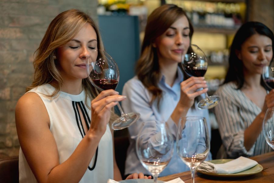 This is an image of three ladies holding a glass of wine up to their noses to smell it.
